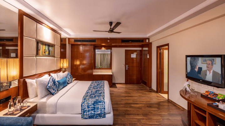 A well-appointed hotel room offers a king-sized bed, a seating area, a television, and wooden flooring.