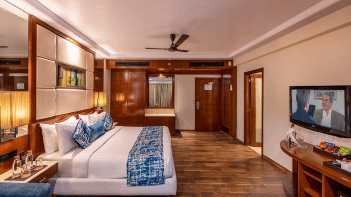 A well-appointed hotel room offers a king size bed, a seating area, a television, and wooden flooring at Libra Lords Inn Jaipur