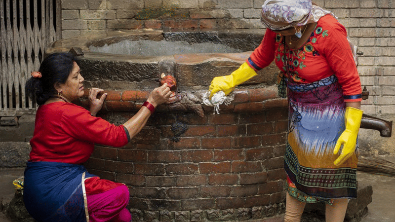 Close-up of local women in colorful clothing scrubbing moss off an ancient community stone well using brushes in Bhaktapur, Nepal.