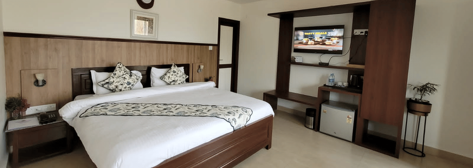 a double bed with side tables, and a tv unit on the side inside one of the rooms - Neer Ganga Resorts