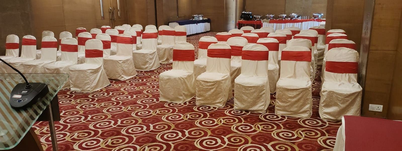 An event space in a hotel with banquet seating and decorative carpet.- The President Hotel Jayanagar, Bangalore