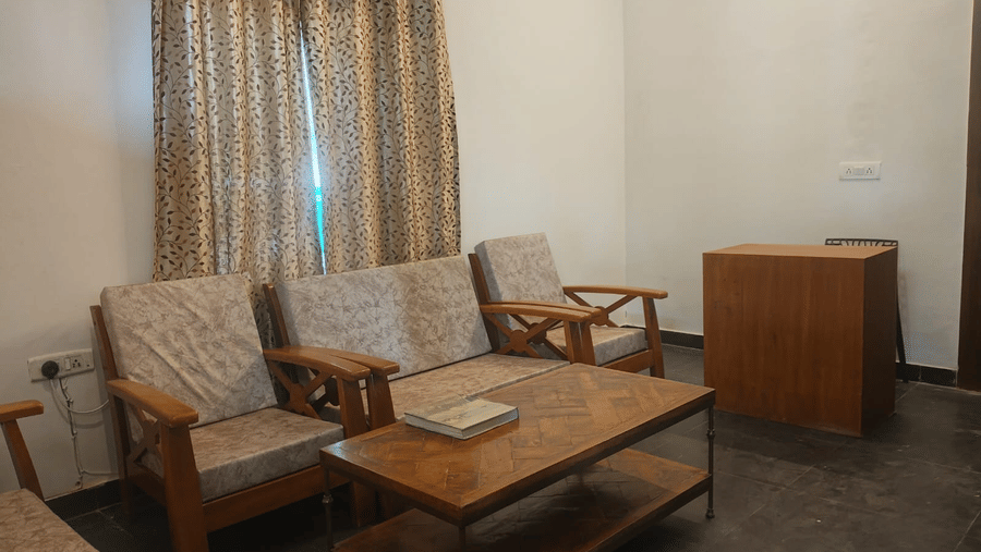  Sitting area with cushioned wooden armchairs, a coffee table, side table and curtained windows.