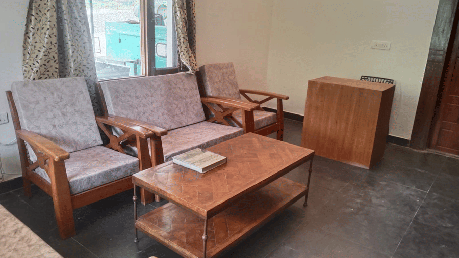 Cosy lounge with wooden armchairs, coffee tables, a side table and windows overlooking greenery.