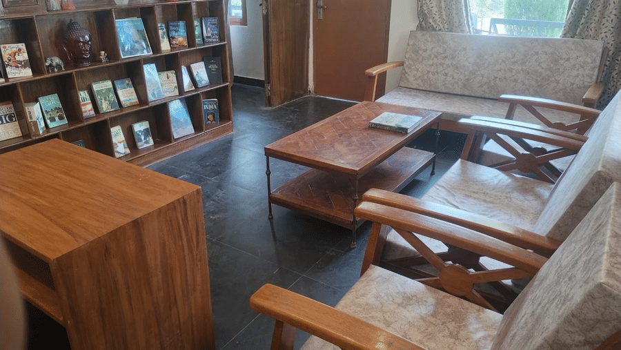 Comfortable lounge with wooden armchairs, coffee tables, bookshelves and large windows overlooking greenery.