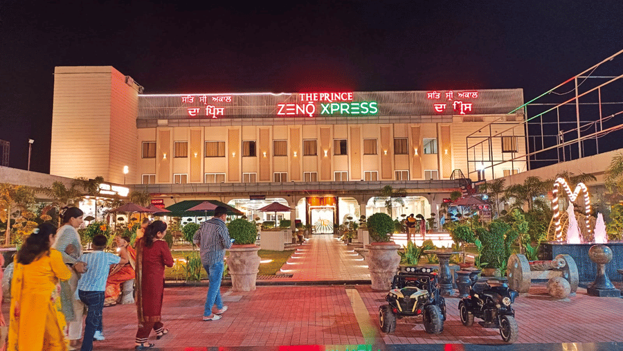 Illuminated facade of the Prince Zenq Xpress Resortt Rohtak, featuring guests entering the premises.