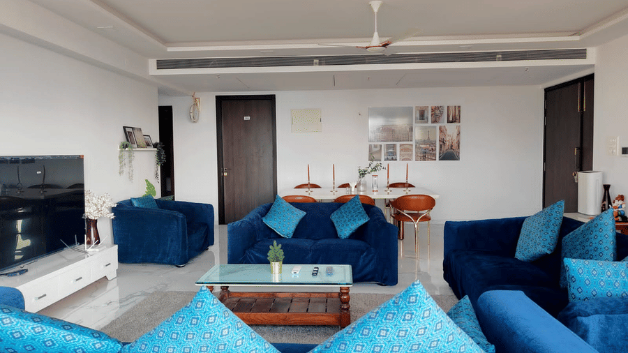 3hall and living room area of Maxxvalue Hotel, Chitranjan Tower, Powai with blue themed couch and a dining table in the corner of the room