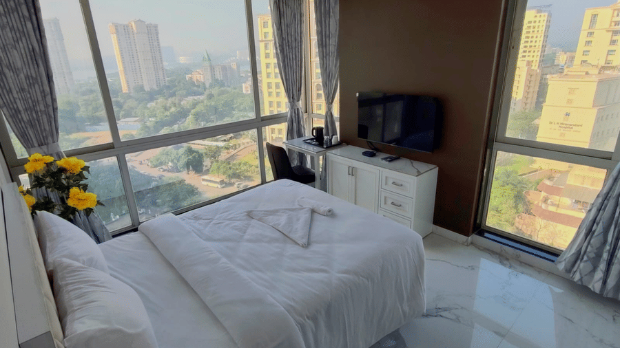 deluxe room at Maxxvalue Hotel, Chitranjan Tower, Powai with a posh bed and white linens along with floor-to-ceiling windows offering ciy view3