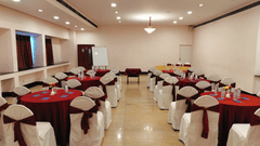 A banquet hall with round tables and chairs covered in cloth at best resort in Bangalore | Ramanashree California Resort