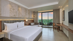 King bed with plush white linens and headboard in the Executive Suite at Sarovar Portico Gir, featuring access to a private balcony.