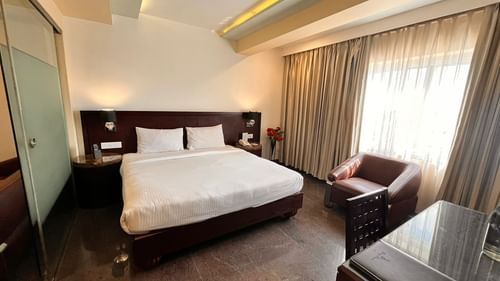 Executive suite room featuring a plush bed with nightstands attached to headboard and a couch placed next to the window