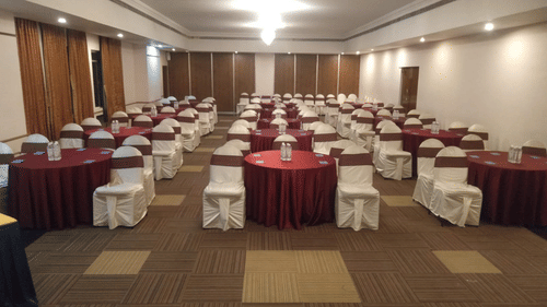 A large banquet hall with rows of round tables and chairs arranged for seating at best resort in Bangalore | Ramanashree California Resort
