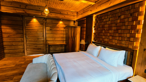 A bedroom at The Baagh Ananta Elite, Ranthambore featuring a king size bed, plush sofa bench, wooden wardrobe, and warm ceiling lighting.  