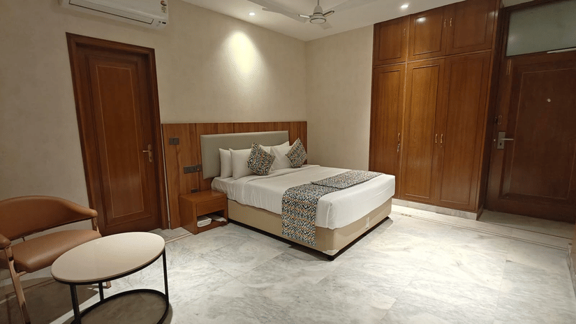 Corner view of a family room highlighting a neatly made bed, cushioned headboard, bedside table, and ambient ceiling lights. The calm colour palette and uncluttered design enhance relaxation and ease of use.