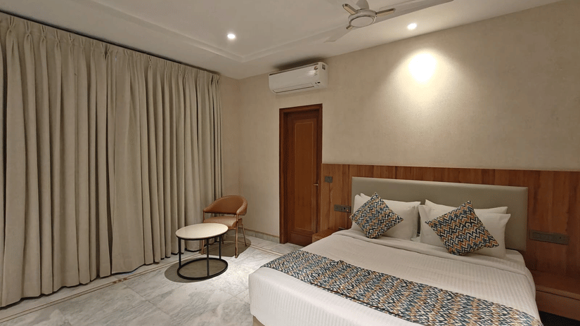 Well-lit family room with a king-size bed, patterned runner, matching cushions, and floor-length curtains. The room’s open design and polished flooring create an airy feel suitable for families seeking comfort and space.