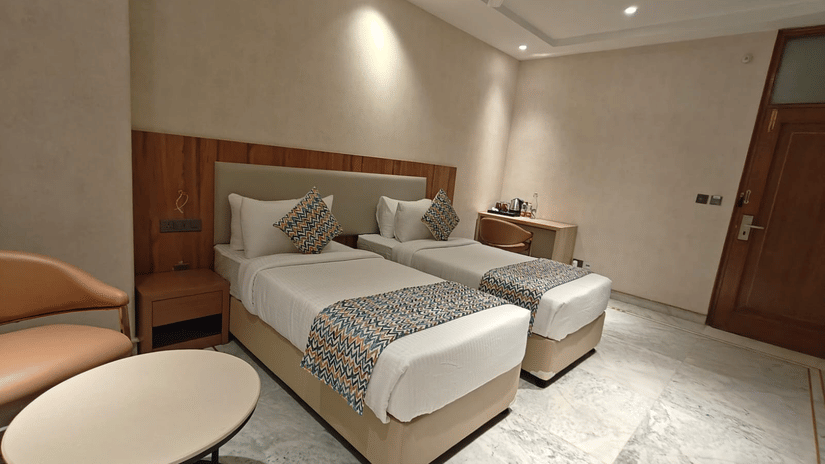 Family room showcasing twin beds with coordinated bedding, a compact seating table, marble flooring, and subtle wall lighting. The room’s neutral palette and organised layout offer a calm and functional setting for multiple occupants.