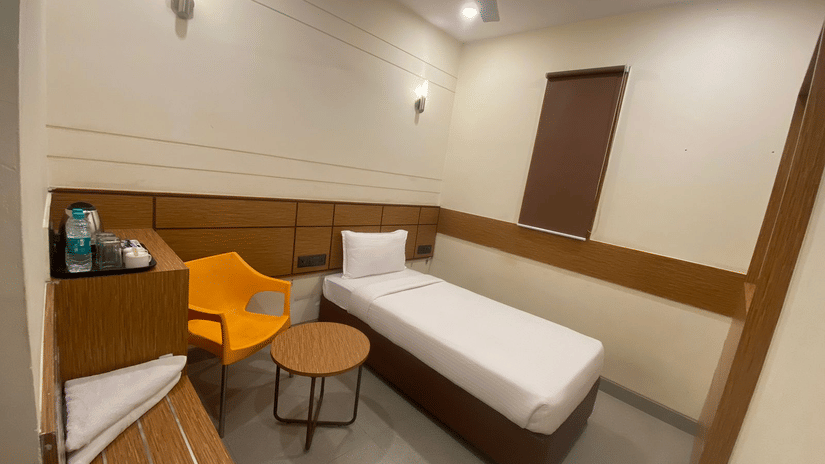 A simple and functional single room, equipped with a single bed, accommodating solo travelers. The room has essential comforts, such as a fan, air conditioning, and a small, colorful chair and table set.