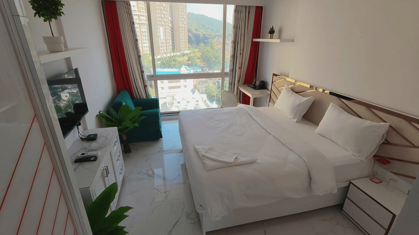deluxe room at Maxxvalue Hotel, Chitranjan Tower, Powai with a posh bed and white linens along with floor-to-ceiling windows offering ciy view1