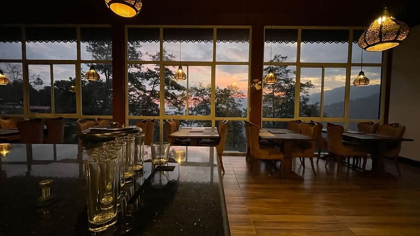 Overview of the Restaurant with seating arrangements and large windows with a view - Sumitel Gangtok