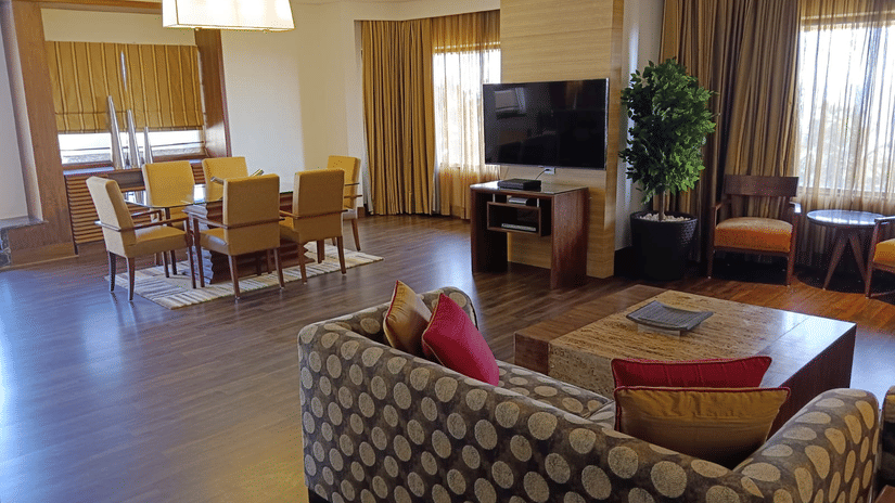 Spacious suite living and dining area at Retreat with patterned sofa wooden flooring a wall-mounted TV and a dining table with yellow chairs in a warmly lit open layout.