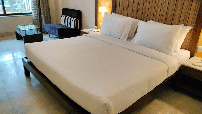 An image of a bedroom featuring a double size bed, a flat TV screen, a dressing table, a  sofa and a centre table - VITS Lonavala.