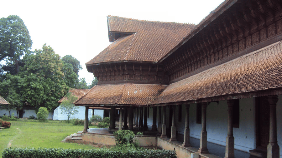 An old building featuring Kerala architecture of slopping roofs and pillars with a green frontyard.