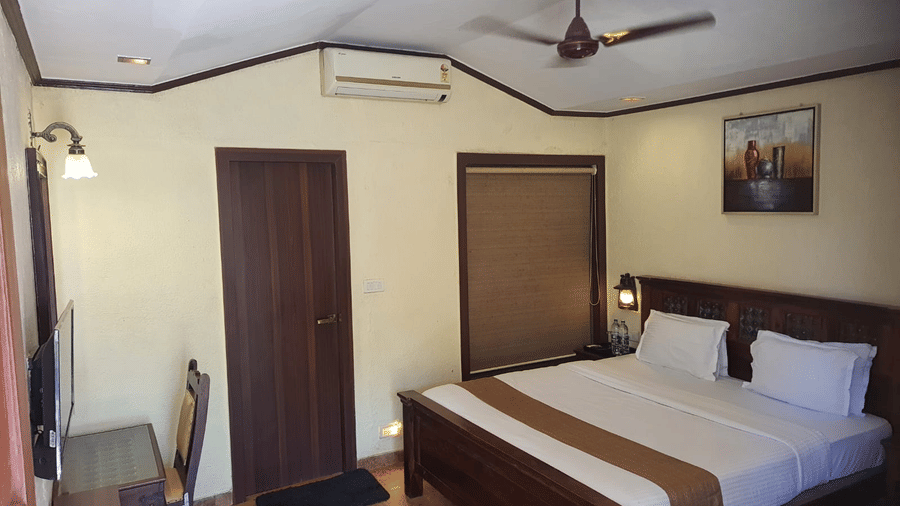 A Super Deluxe room featuring a dark wood double bed, matching door, glass desk, and clean tiled floors.