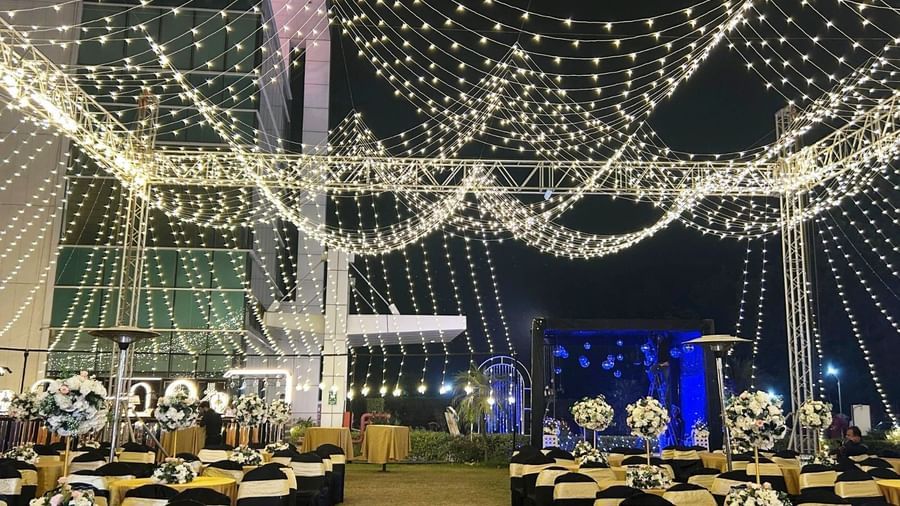  An outdoor nighttime event at Amer Greens with rows of tables set up on grass, all underneath a canopy of draped string lights.