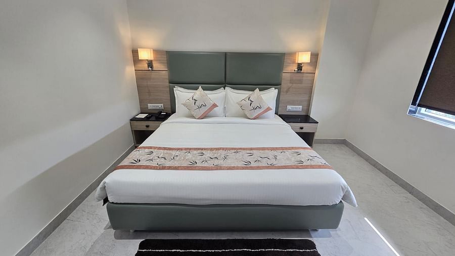 A deluxe room in Clarks Inn Express, Firozbad, featuring a nealty made king size bed with patterned runner, and a floor rug.