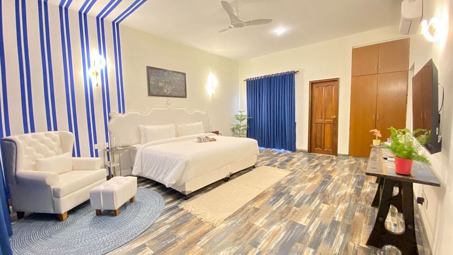 A King sized bed with soft mattress and pillows and a single sofa with foot support, with a flat TV, a nailed art on the wall, along with a huge portion of the room painted with blue stripes.