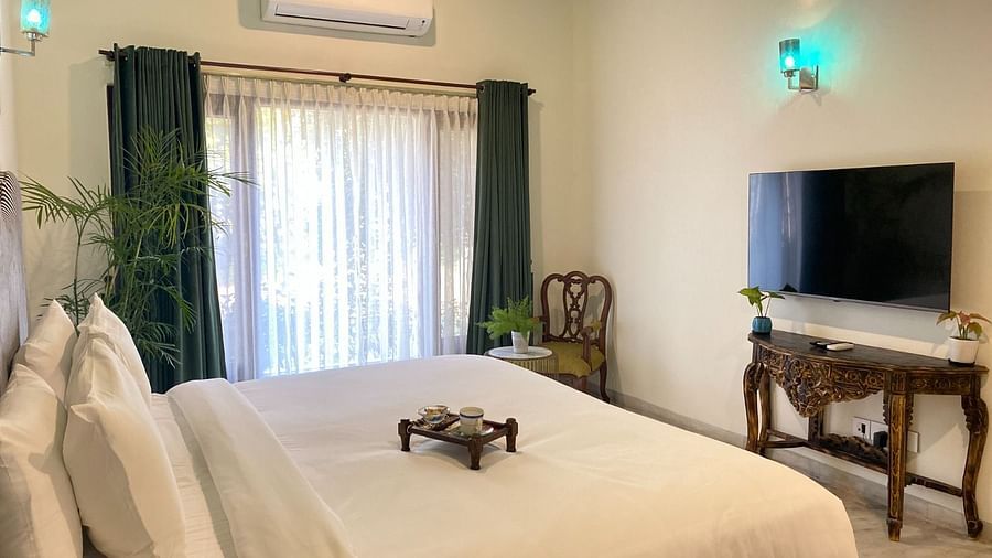 An image showing the King sized bed with lush mattress and pillows and a corner chair, and a Flat TV, with a balcony covered by the curtains present