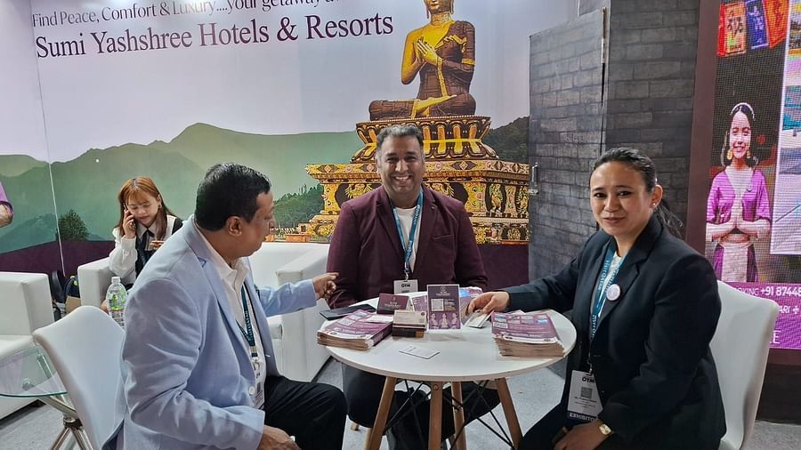 Three individuals seated at a round table in a booth promoting Sumi Yashshree Hotels & Resorts. 