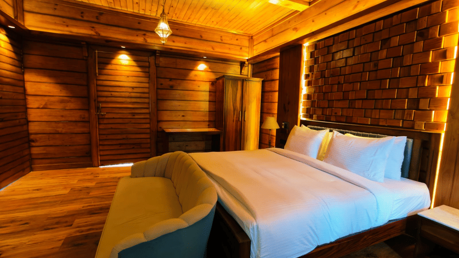 A bedroom at The Baagh Ananta Elite, Ranthambore featuring a king size bed, upholstered sofa bench, wooden wardrobe, and textured brick accent wall.  