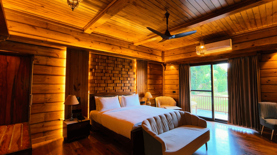 A bedroom at The Baagh Ananta Elite, Ranthambore featuring a king size bed, upholstered bench, single armchair, and glass door leading to a balcony.