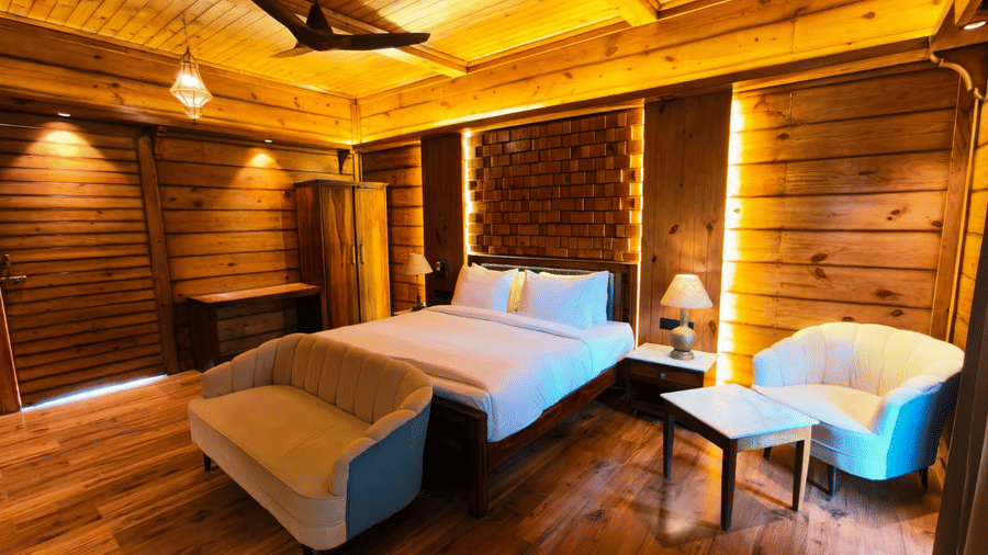 A bedroom at The Baagh Ananta Elite, Ranthambore featuring a king size bed, upholstered bench, single sofa, and small coffee table.  