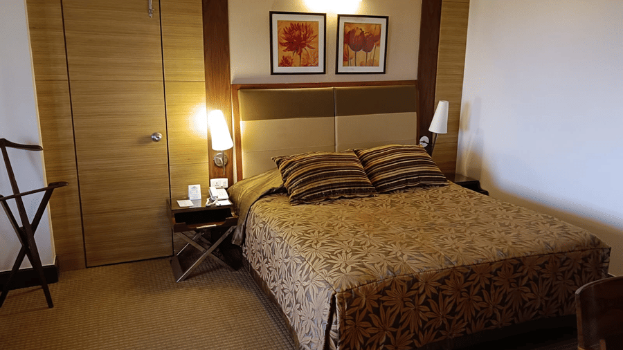 A bedroom featuring a patterned bedspread, coordinating pillows, framed floral artwork above the headboard, and a door on the left side - The Retreat Hotel and Convention Centre