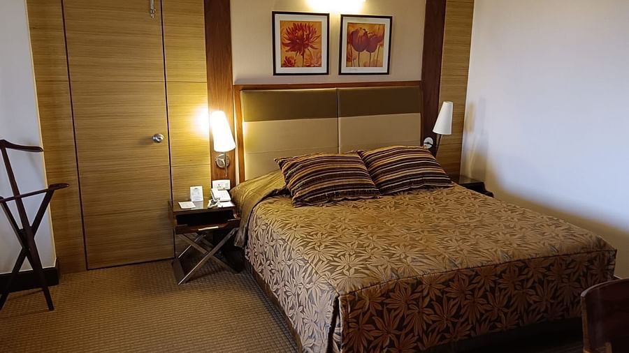 A hotel bedroom featuring a patterned bedspread, coordinating pillows, framed floral artwork above the headboard, and a door on the left side - The Retreat Hotel and Convention Centre