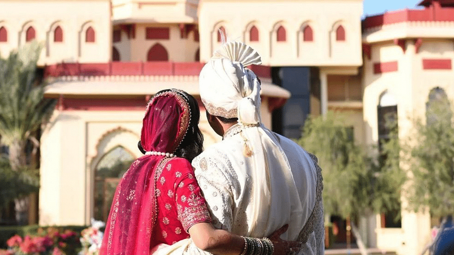 bride & groom in traditional Indian attire, standing in front of The Ummed Jodhpur Palace.