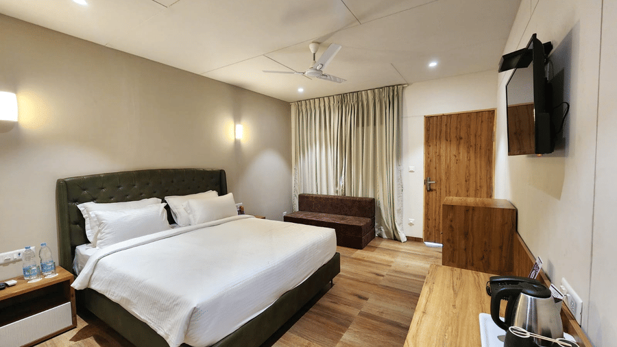 An overview of the Cottage in Daman's interior with ceiling fan, a double bed, wall mounted bed lights, a TV and much more in view at VITS Daman Devka Beach.
