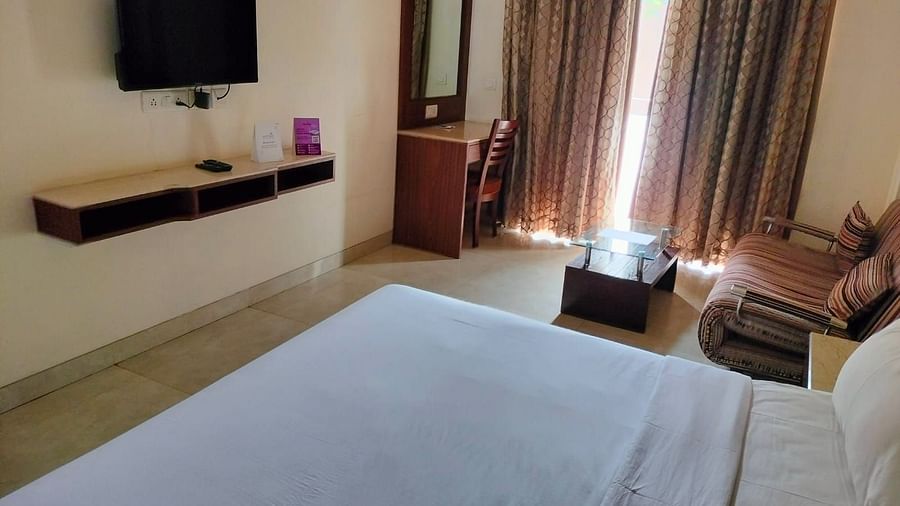 An image of a bedroom featuring a double size bed, a flat TV screen, a dressing table, a  sofa and a centre table - VITS Lonavla