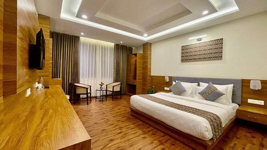 A full view of a room that has a bed, TV on the wall, wooden desk, and two chairs | Voyage The Royal Retreat, Gangtok
