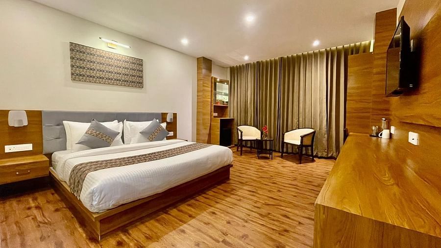 A full view of a wooden-floored room that has a bed, two chairs, and a TV on the wall | Voyage The Royal Retreat, Gangtok