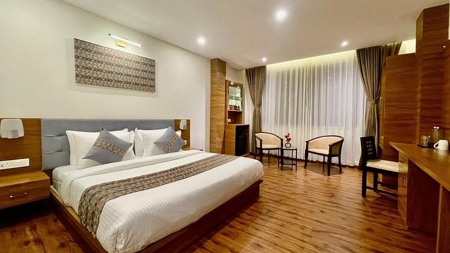 A wooden-floored room that has a bed, two chairs, and a TV on the wall | Voyage The Royal Retreat, Gangtok