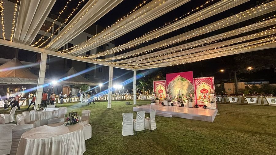 A night-time view of an event setup on a lawn with decorative lighting and round dining tables under a canopy.