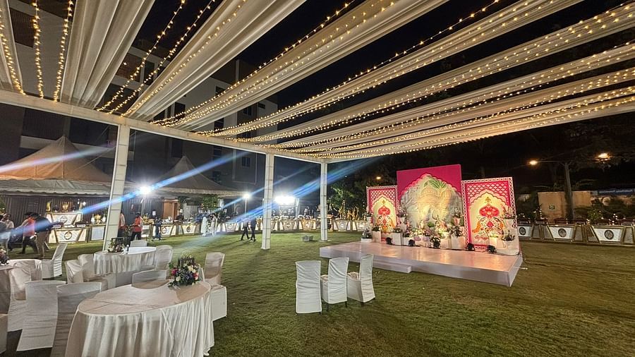 Canopy-covered outdoor event area featuring a stage with vibrant floral backdrops and round dining tables on the lawn.