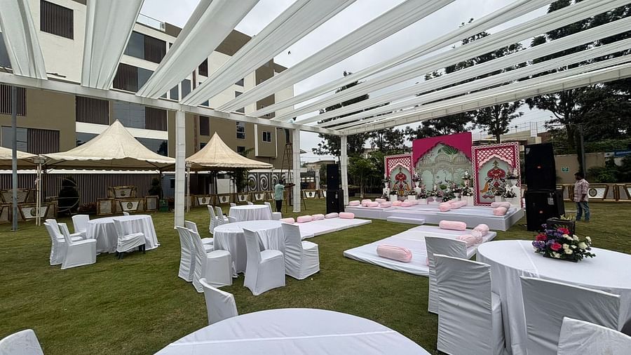 A wide-angle view of an outdoor event setup with white canopies, dining tables, and a floral stage in the background.