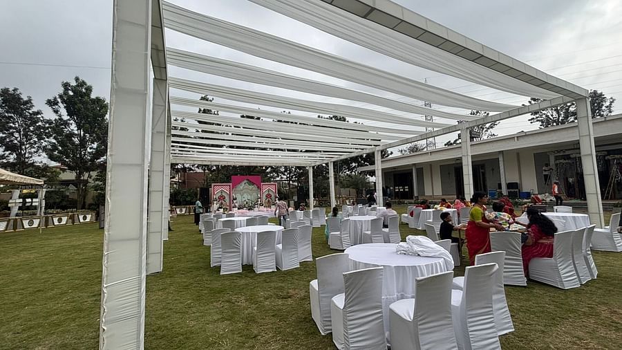  Daytime view of an outdoor dining area featuring a white canopy, round tables, and chairs on a lawn.