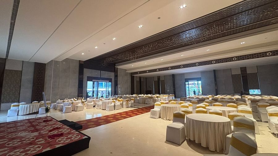 A banquet hall with luxurious decor, featuring round tables, cream-coloured chairs, and a stage setup.