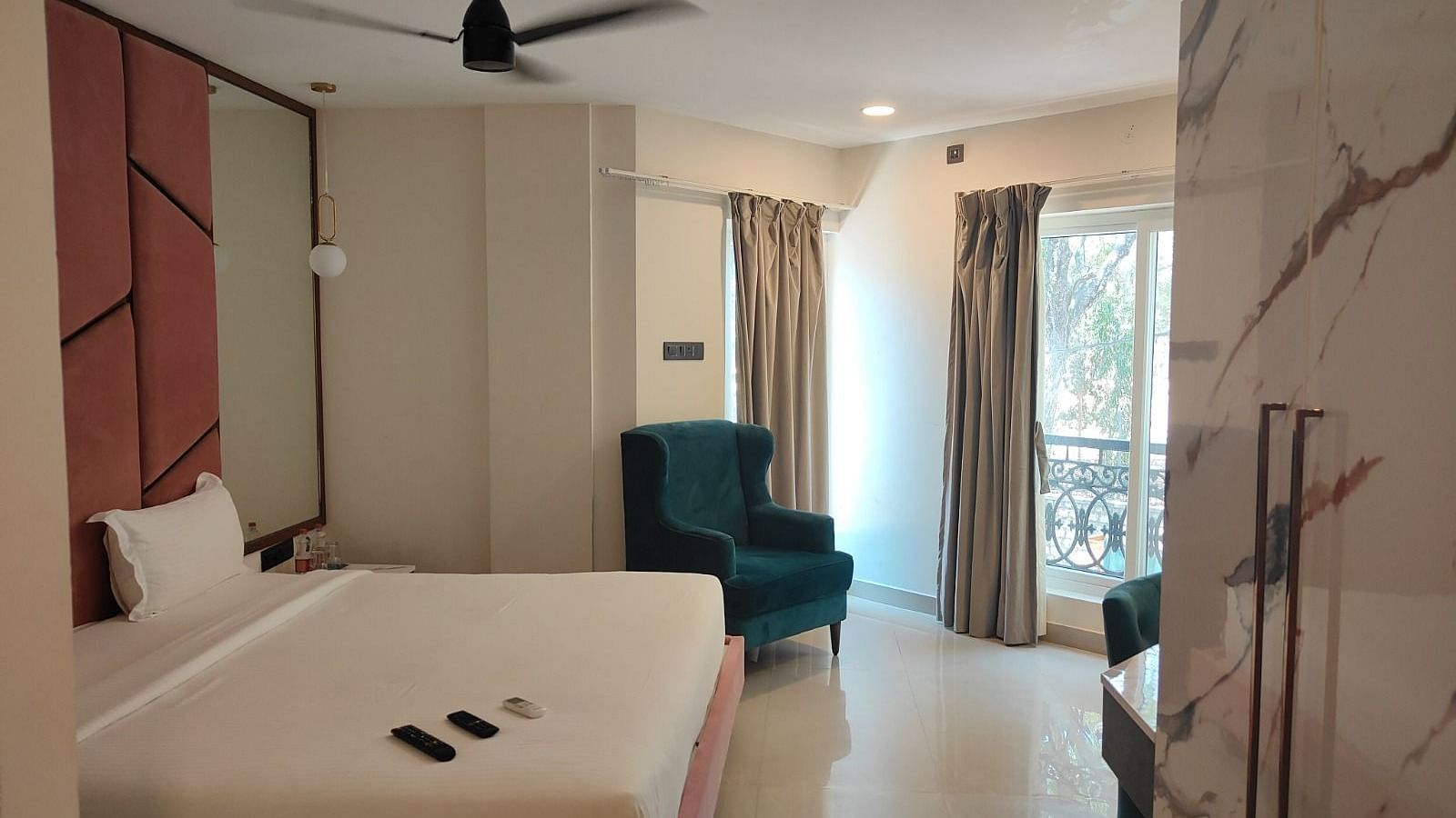 a plush double bed and a teal coloured cushioned arm chair at the junior suite - Astra Hotels and Suites, Koramangala
