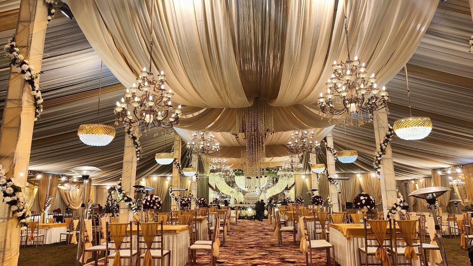 A beautifully decorated wedding hall with chandeliers, draped fabric, and tables set for guests.