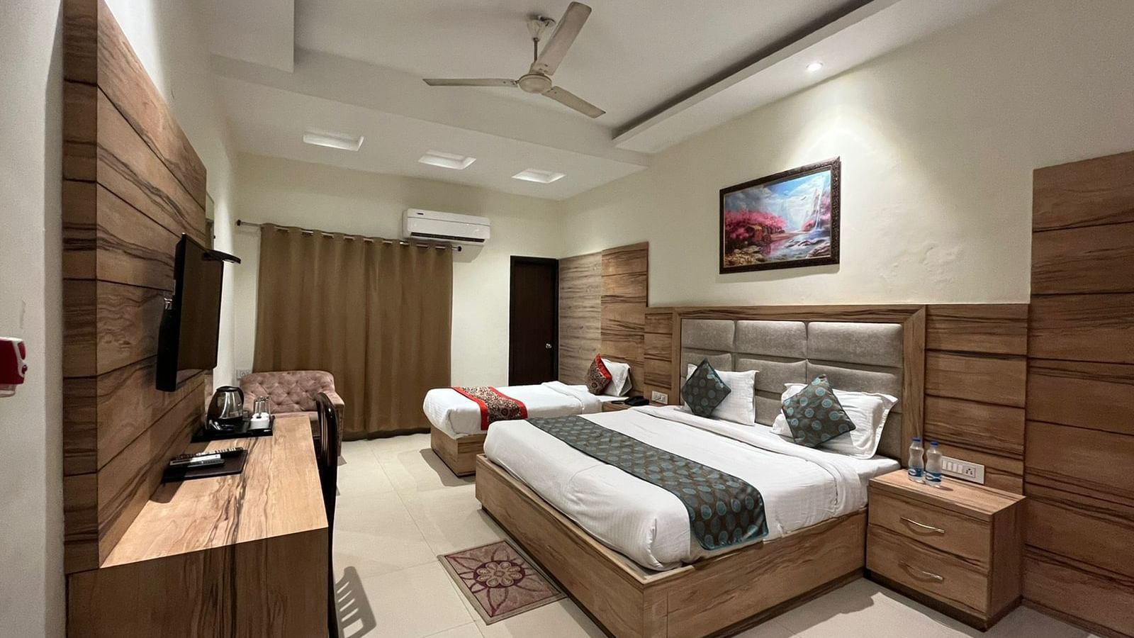 A clean, modern hotel room with a single queen-sized bed, a wooden headboard, and a flatscreen TV mounted on the wall.